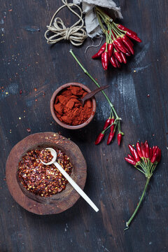 Bunches of red chili peppers, cord plate of chili flakes and bowl with chili powder on wood