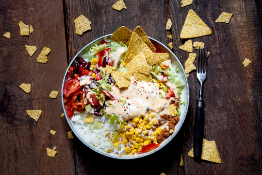 Taco salad bowl with rice, corn, chili con carne, kidney beans, iceberg lettuce, sour cream, nacho chips, tomatoes