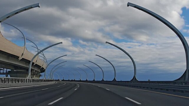 View from car driving on highway bridge with curved street lamps under dramatic cloudy sky, dashboard perspective of road trip, urban transport, travel journey