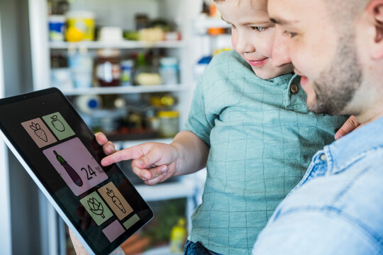 Father and son use a food app on a tablet in the kitchen