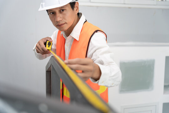 inspector or engineer is inspecting construction and quality assurance check dimension of house by using a tape measurement. Engineers or architects or contactor work to build the house before sell.