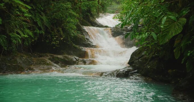 Cascading stepped waterfall flows into a vibrant turquoise pool in deep jungle setting of Costa Rica