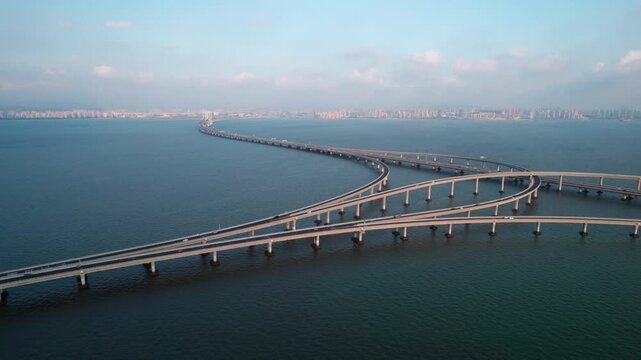 A long elevated sea bridge with interchange sections spanning calm blue water, connecting coastal urban areas under a clear sky.