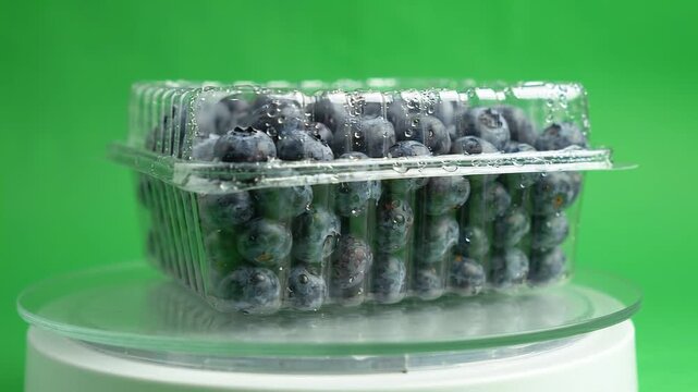 Transparent plastic clamshell container filled with fresh blueberries rotating on glass
