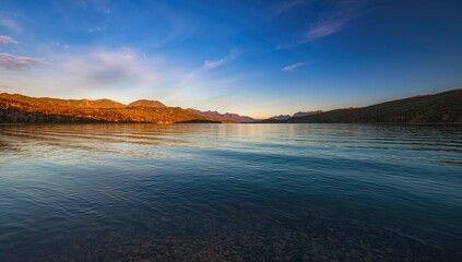 Obraz premium Serene Mountain Lake at Sunrise with Calm Water Reflection and Clear Blue Sky