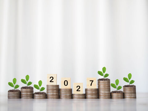 Financial growth concept with wooden blocks spelling 2027 and small plants on coins