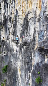 Vertical Video: A climber moves along a via ferrata route on a karst cliff, suspended above the valley below