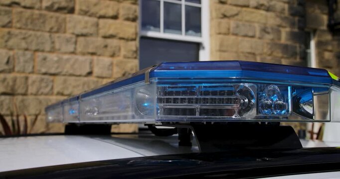 Close up slow motion footage of white and blue emergency lights mounted on the roof of a British police vehicle with the detailed LED light bar shown against a traditional stone building