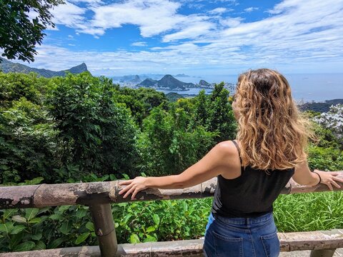 Woman enjoying the panoramic view of Rio de Janeiro, including Christ the Redeemer and Sugarloaf Mountain, from the lush Tijuca Forest in Brazil.
