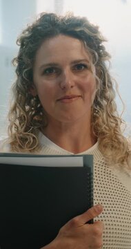 Portrait of Happy Smiling Female Teacher Holding Notebooks and Folders Standing in School Corridor with Lockers. Mentorship, Academic Support, Positive Communication in Modern School. Vertical Shot.