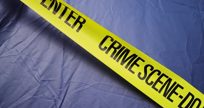 Slow motion footage of bright yellow crime scene do not enter barrier tape with bold black warning text stretched diagonally across a dark blue fabric background representing police investigation