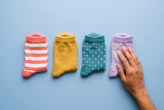 Four odd socks in a row and a hand smoothing the last one, individuality, inclusion and being different