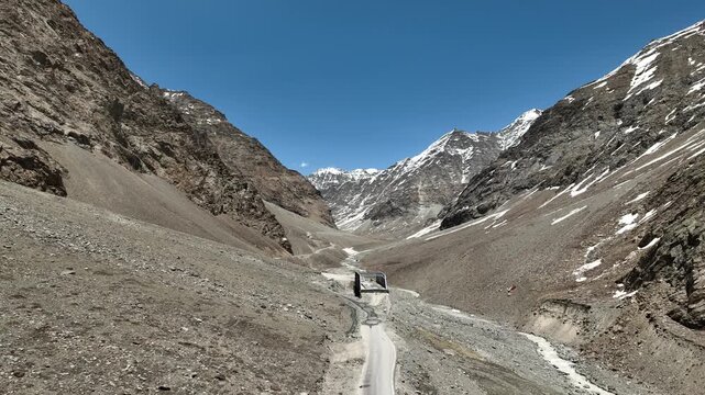 Aerial view of rocky valley with drone flying towards massive snow-capped mountains and a dirt road in Zanskar Ladakh India shot by a drone moving along the road