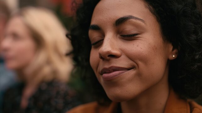 Close up of a woman with dark curly hair wearing a brown top, eyes closed in contentment