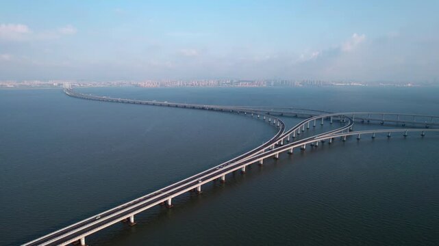 A long concrete bridge spans across calm blue water, with interchange ramps under a clear sky.