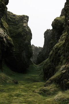 Dark moss covered cliffs frame a narrow green ravine beneath an overcast sky, creating a remote autumn wilderness scene.