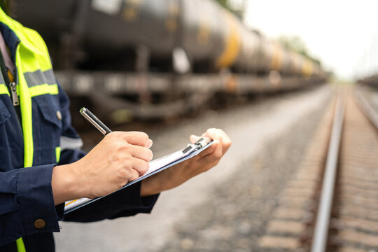 A safety officer is checking on hazardous chemical material checklist for risk assessment before tranportation the dangerous good with train tanker railway background. Industrail working scene.