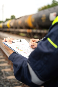 A safety officer is checking on hazardous chemical material checklist for risk assessment before tranportation the dangerous good with train tanker railway background. Industrail working scene.