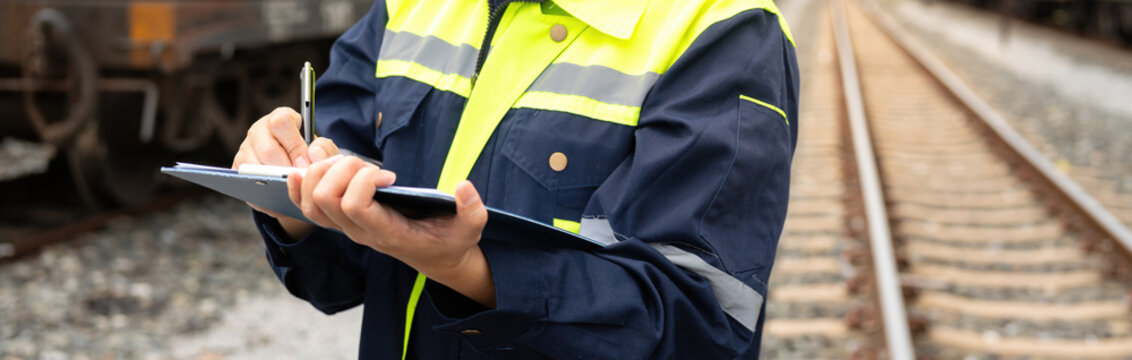 A safety officer is checking on hazardous chemical material checklist for risk assessment before tranportation the dangerous good with train tanker railway background. Industrail working scene.