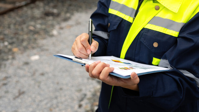 A safety officer is checking on hazardous chemical material checklist for risk assessment before tranportation the dangerous good with train tanker railway background. Industrail working scene.