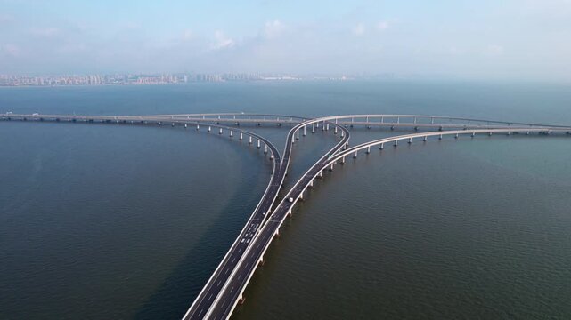 An aerial view of a multi-way road bridge spanning across calm coastal waters, connecting two distant urban areas.