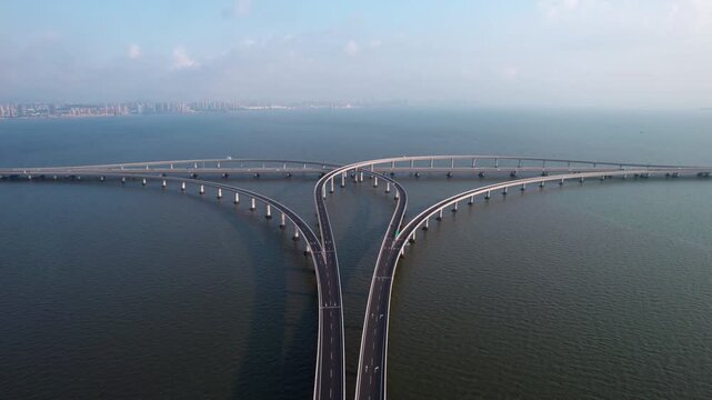A large curved sea bridge with multiple road spans extends over calm water under a clear sky.