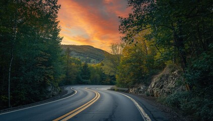 Naklejka premium Curving Road Surrounded by Autumn Trees under a Colorful Sunset Sky
