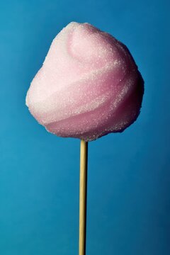Soft and fluffy pink cotton candy on a stick set against a vibrant blue backdrop