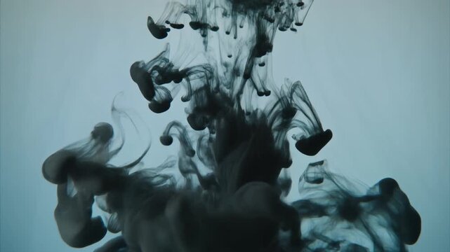 Dynamic dark pigment swirls and disperses fluidly within a luminous pale blue liquid, creating mesmerizing abstract shapes and organic patterns with captivating visual motion