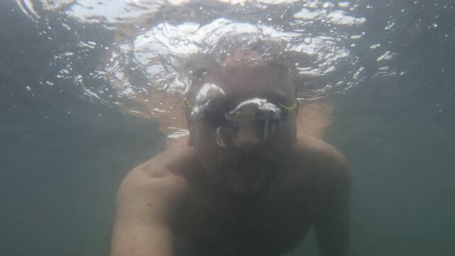 Man holding breath and swimming underwater with goggles, enjoying water sport activity and summer vacation