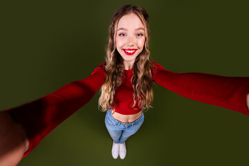 Naklejka premium Young woman in red crop top jeans smiles with outstretched arms against a green background for a bright fashion lifestyle photo