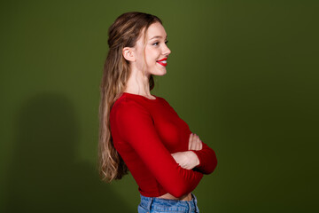 Fototapeta premium Confident young woman in red top smiles with arms crossed against green studio backdrop
