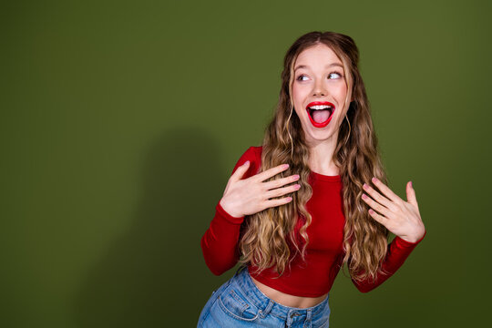 Young woman in red top laughing with hands on chest against green studio background