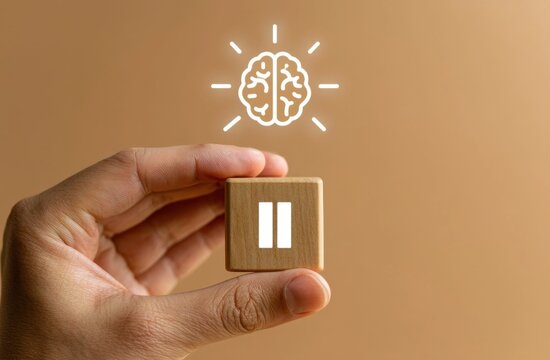 Human hand holding a square pause button with a glowing brain above it