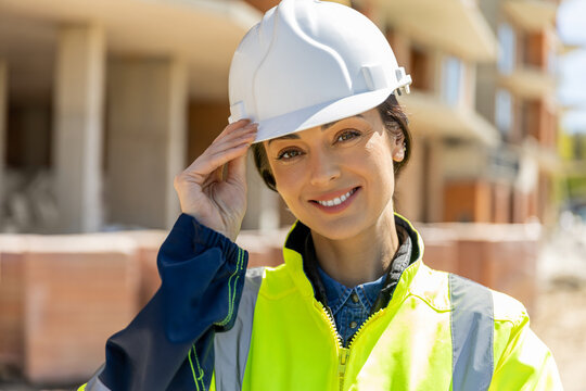 Young female contractor wearing safety vest adjusting white helmet