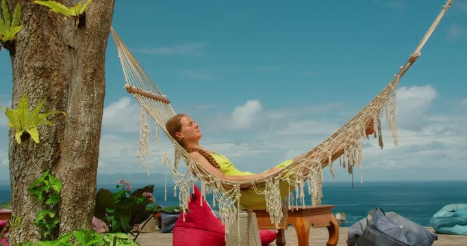Calm woman lying in a macrame hammock enjoying the tropical breeze and coastal island scenery