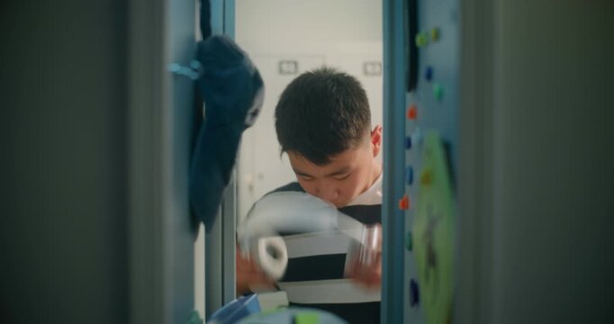 Viewed from inside School Locker, Teenage Student Opens Door, Reaches for Smartphone, Listens to Music Through Wireless Headphones, and Chats. Modern Youth, Technology, and Authentic School Life.