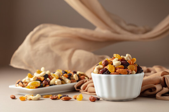 The mix of various nuts and raisins in a white bowl on a beige background.