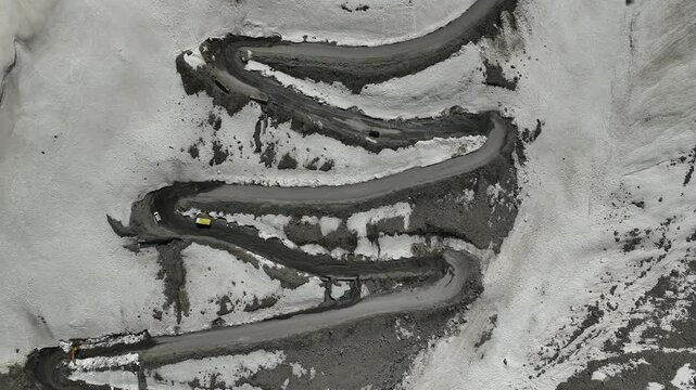 Aerial view of two cars navigating sharp hairpin loops on a highway in snow-covered mountain slopes at Shinku La Pass Zanskar shot by a drone flying above the loops
