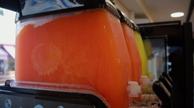 Dispenser full of orange frozen slush, offering a cold and refreshing drink for summer. Condensation on container