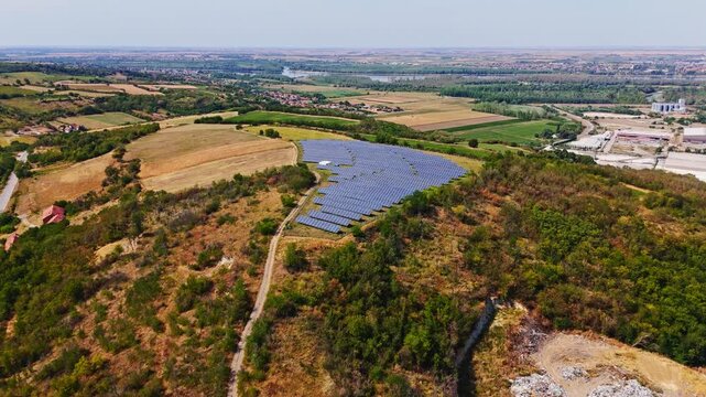 Aerial view of a solar farm situated on a hillside with surrounding rural landscape and trees in Beocin, Vojvodina, Serbia.