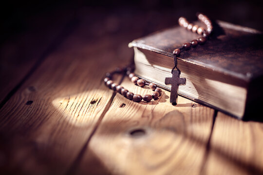 Praying with wooden rosary beads crucifix cross on Holy Bible background