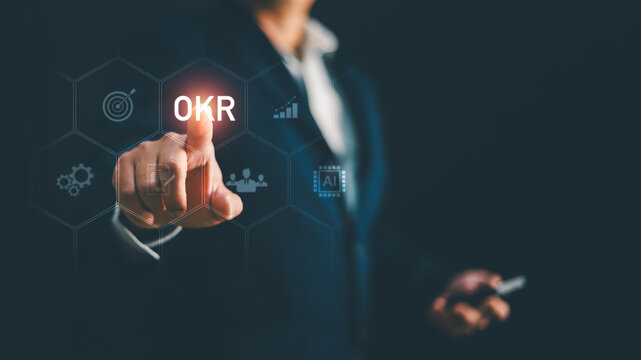 Businessman touching OKR text on futuristic screen with target graph icon. Concept for business goal management, objective key result, strategic planning, performance tracking, corporate success