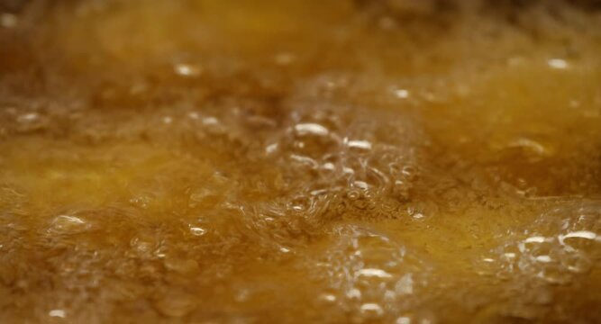 Macro view of golden food frying in bubbling hot oil inside commercial kitchen fryer. Concept of cooking tutorials, restaurant menus and food service ads.