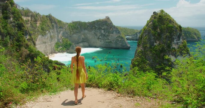 Traveler woman walking on cliff edge overlooking turquoise ocean and Diamond Beach bay in Nusa Penida Bali