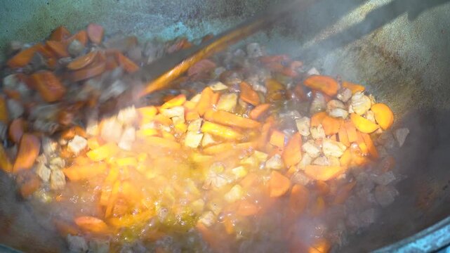 Frying vegetables with meat in oil to make pilaf