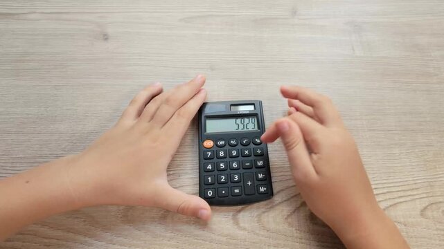 Child Hands Pressing Buttons on a Calculator at a Wooden Table