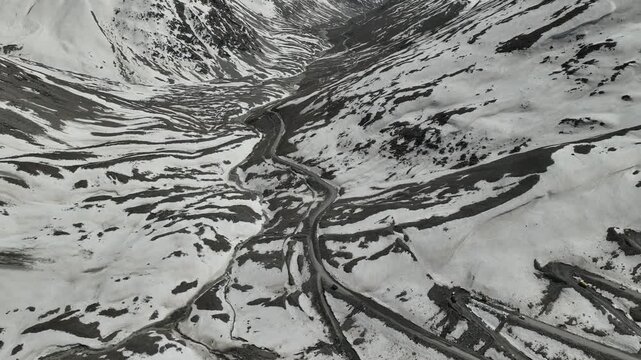 Aerial view of vast open valley with a dirt road leading towards snow-covered mountain ridges at Shinku La Pass Zanskar shot by a drone

