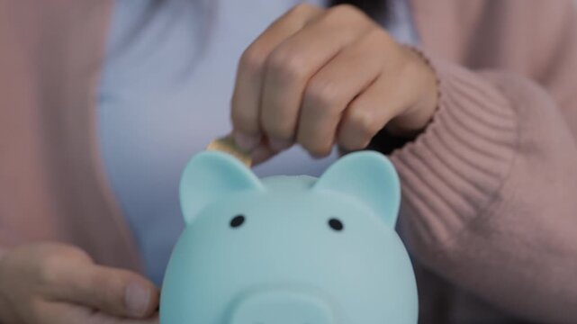 Saving money and financial concept. Close up of woman putting money coins saving in blue piggy bank for investment mutual fund finance and business. 