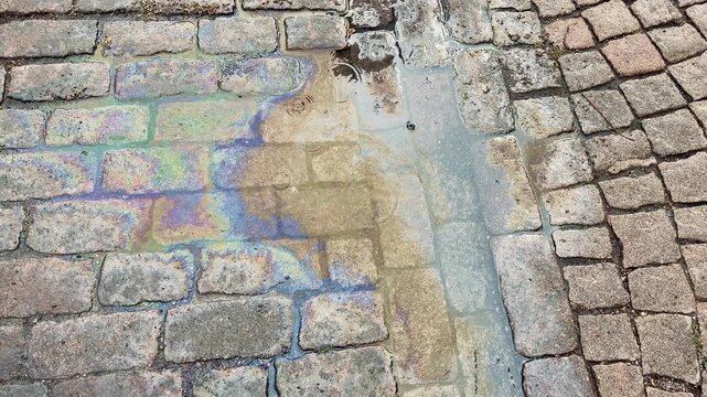 Iridescent Oil Film Spreading on Wet Cobblestone Street